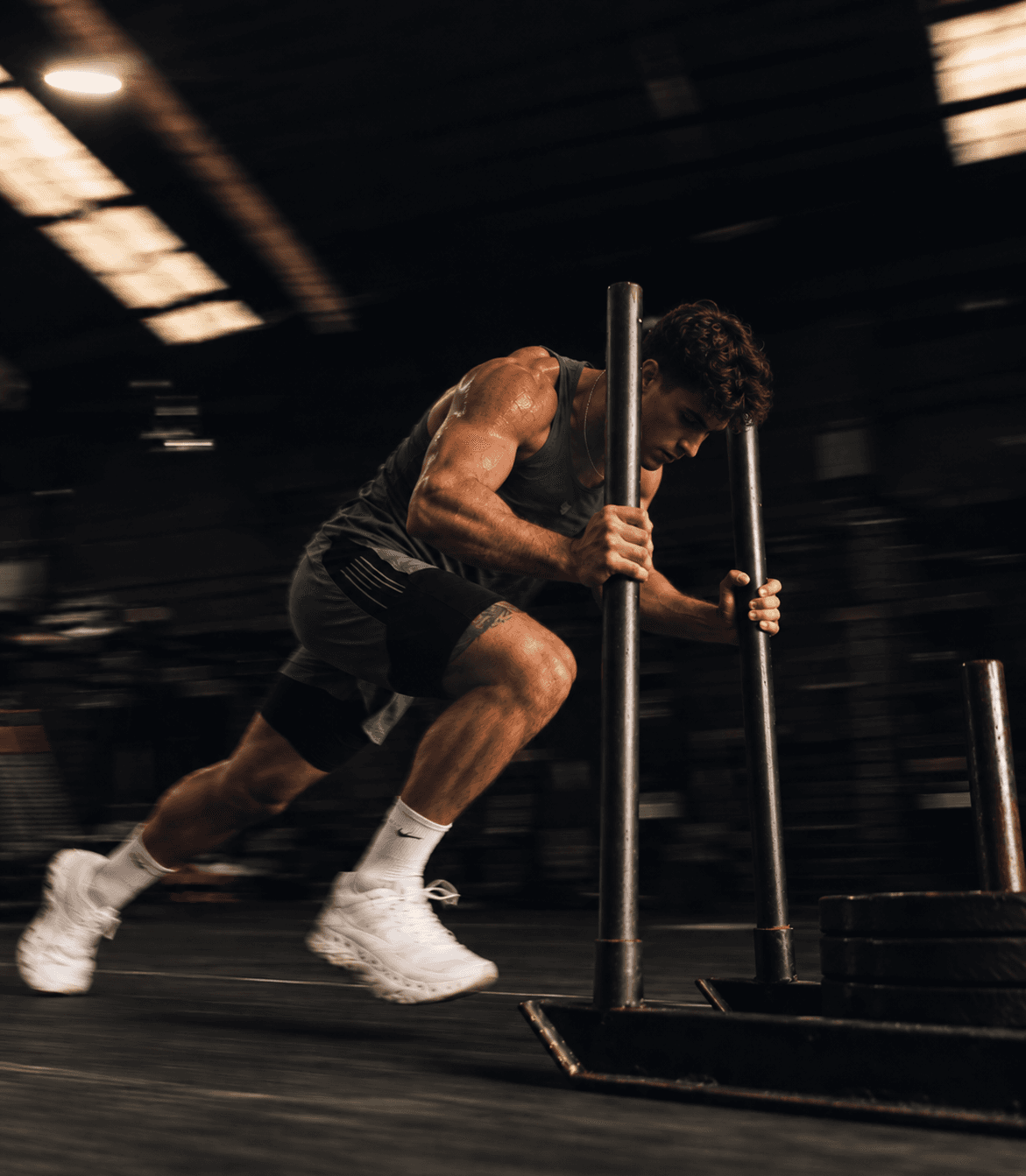 An athlete pushing a sled at full effort in a dark warehouse gym