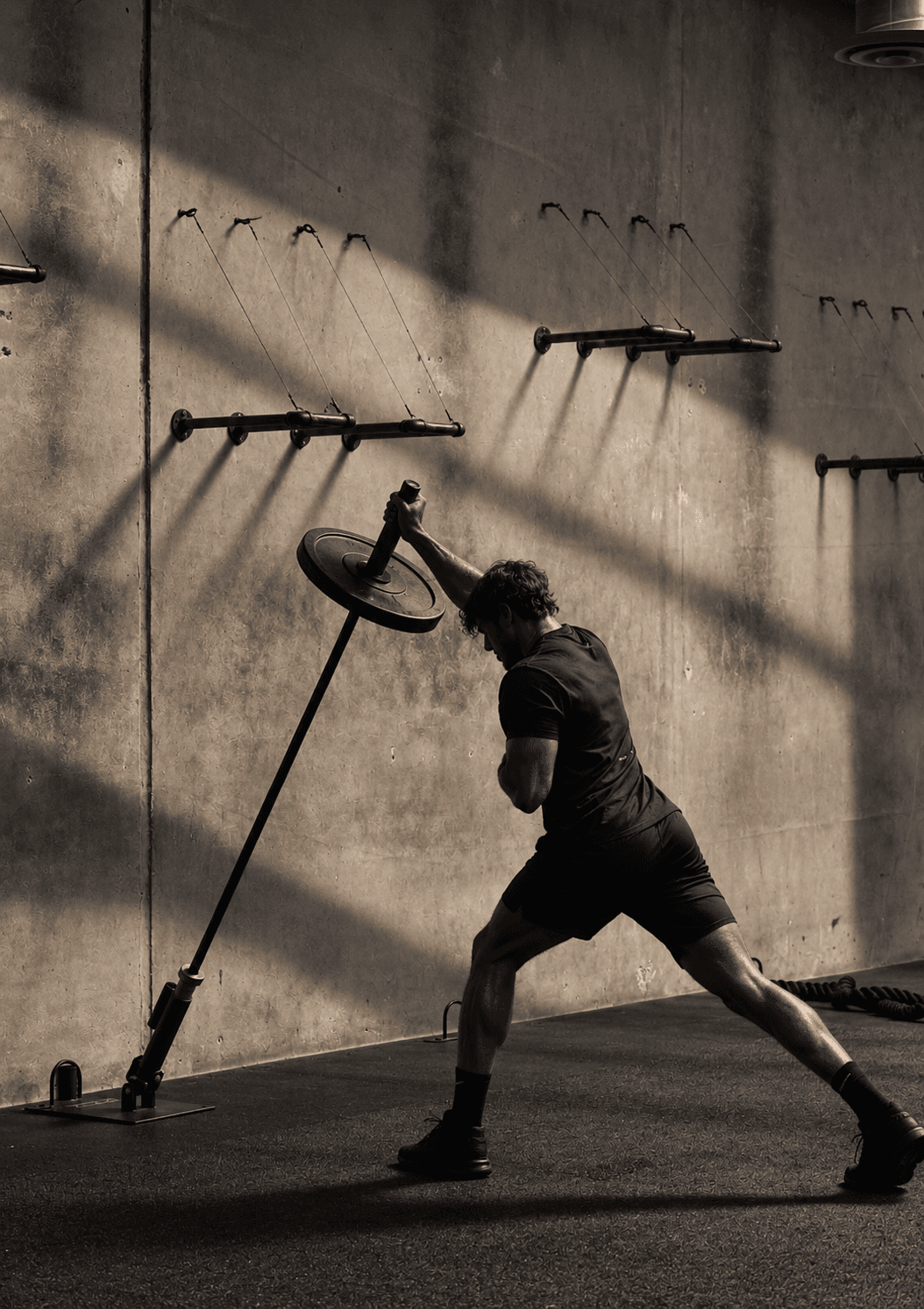 A lifter driving a landmine barbell press against a sunlit concrete wall